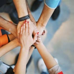 groep jongeren die de handen over elkaar legt in een cirkel